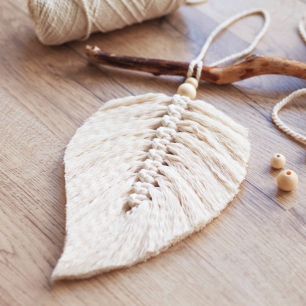 istock Macrame leaf  in natural color and thread windings lying on a wooden table. Cotton rope decor macrame to make your room more cozy and unique. Woman hobby. Handmade wall hanging decor. 1367163677