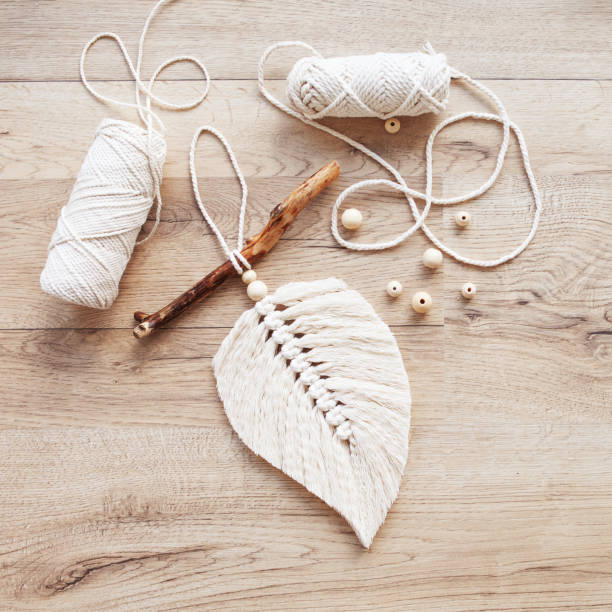 istock Macrame leaf  in natural color and thread windings lying on a wooden table. Cotton rope decor macrame to make your room more cozy and unique. Woman hobby. Handmade wall hanging decor. Copy space 1367163714