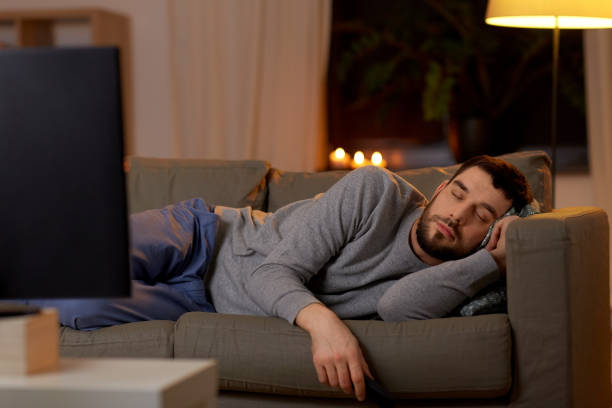 man sleeping on sofa with tv remote at home stock photo