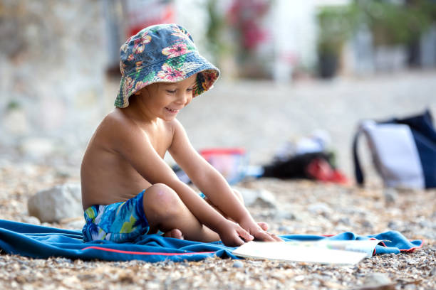 Cute blond toddler boy, reading a book on the beach