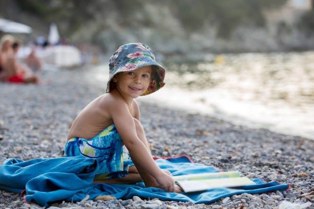 istock Cute blond toddler boy, reading a book on the beach 1367164496