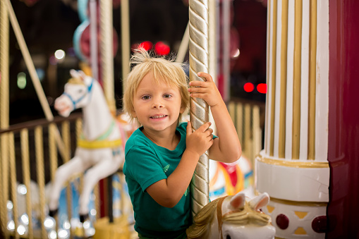 Sweet child, cute blond boy, riding on a merry-go-round, carousel attraction in Europe, active children, night time