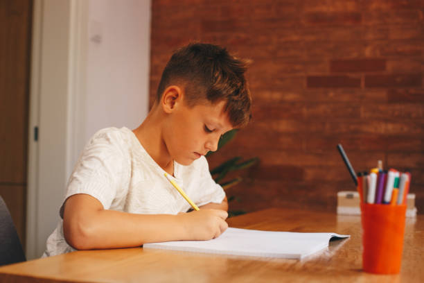 istock A young boy in a white T-shirt is sitting at the table, writing down his homework. 1367165334