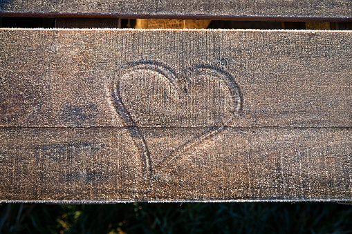 A close up, high angle shot of a heart drawn into frost on a plank of wood.
