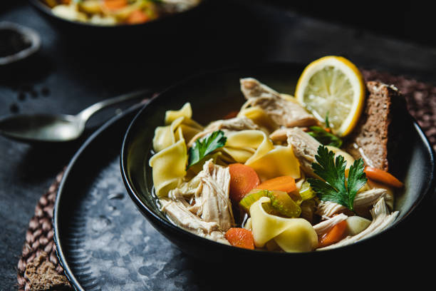 Freshly made chicken noodle soup with edd noodles served on black table. Chicken broth with wholegrain bread slice over a table.