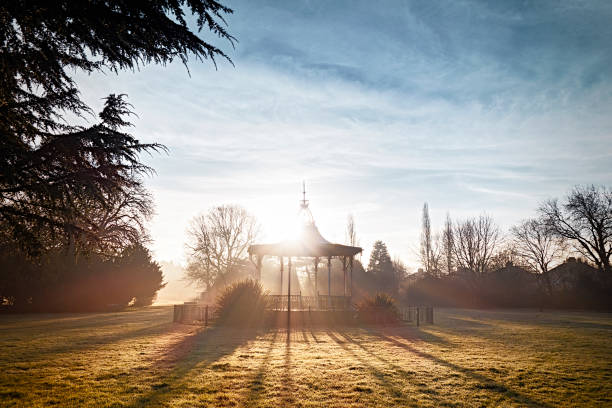 A park bandstand, early on a frosty, slightly misty, winter morning with the sun rising behind the old bandstand in Beckenham Recreation Ground in Beckenham, Kent (South East London). Thought to be the only one of its kind still in existence, the bandstand is Grade II listed but was falling into disrepair at the time this photograph was taken: it has since been restored to its Edwardian splendour. The bandstand was where David Bowie (who lived in Beckenham at the time and who started his career in the town) performed at a free festival which he compèred and helped to organise in 1969. It is locally known as the “Bowie Bandstand”.
