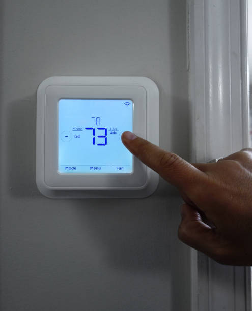 persona que ajusta la temperatura del hogar en un termostato inteligente - termostato fotografías e imágenes de stock