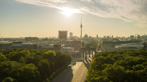 The Brandenburg Gate in Berlin in the summer sunrise at the Golden Hour. In the background the Hotel Adlon and the Berlin TV Tower. Long focal length recording.