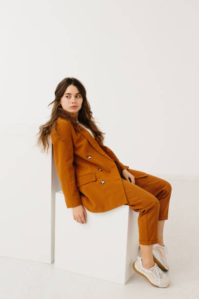 istock Young woman in trendy pastel suit sitting on cube against white background 1367181749