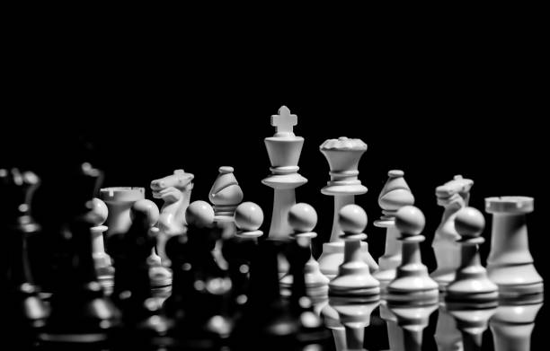 istock Close up of Chess pieces on a reflective mirror board surface with black background 1367184829