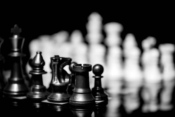 istock Close up of Chess pieces on a reflective mirror board surface with black background 1367184952