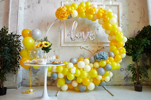 Photo zone for a photo session. Yellow and gray balloons are collected in an arch. Aero design and candy bar with sweets for a festive event.