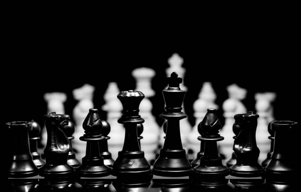 istock Close up of Chess pieces on a reflective mirror board surface with black background 1367187519