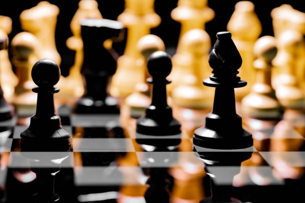 istock Close up of Chess pieces on a reflective mirror board surface with black background 1367188345