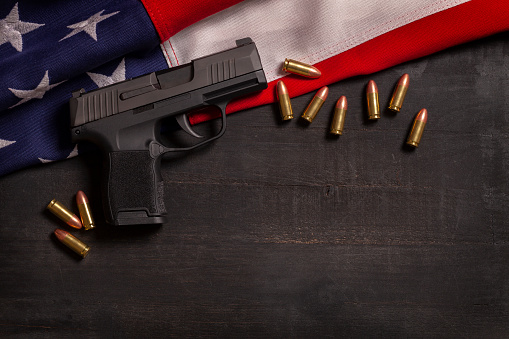 Pistola negra y balas con una bandera estadounidense sobre un fondo pintado de madera negra photo