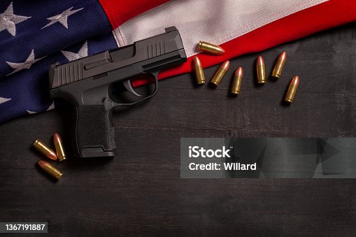 istock Black pistol and bullets with an American flag on a black wood painted background 1367191887