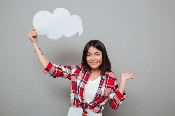 istock Smiling woman holding speech bubble over grey wall. 1367199694