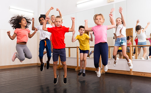 Group of cheerful tweens jumping with female trainer during modern dances class