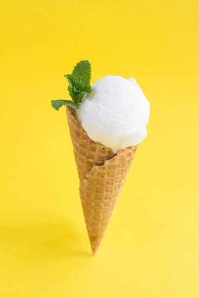 istock Close-up on vanilla ice cream in a waffle cone on the yellow background 1367201230