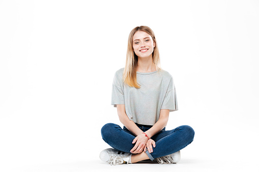 Young blonde smiling woman sitting cross-legged isolated over white