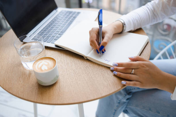 istock Close-up view of a woman's hands writing notes in a notebook. Girl working in a cafe 1367203356