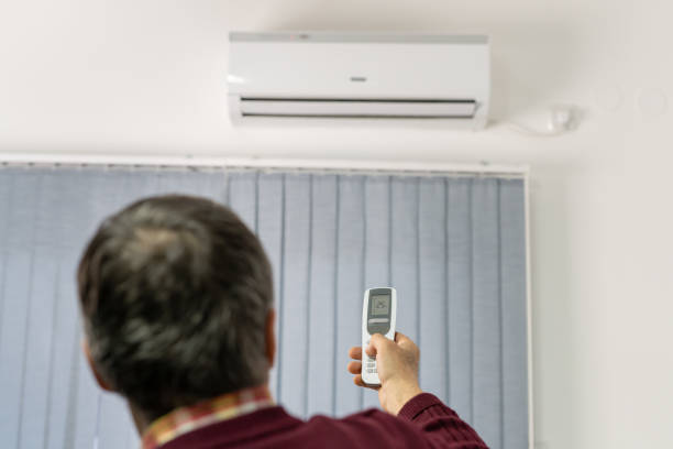 istock Back view of one caucasian senior man holding remote controller to adjust air-condition temperature in his apartment at home real people copy space 1367206412