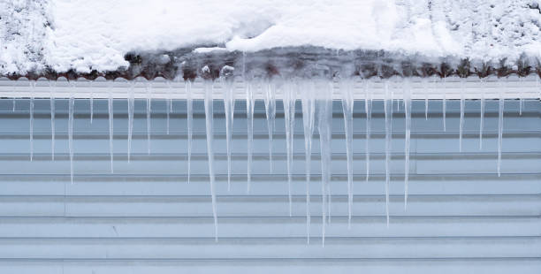 istock Several icicles hang from the roof against a gray plastic siding wall. Cloudy winter day. Background. 1367206671