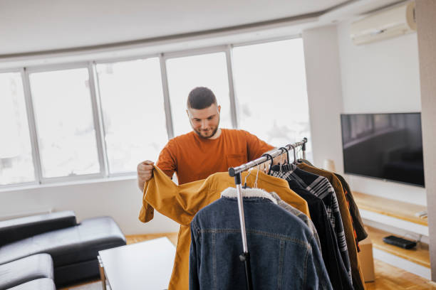 istock Young man selecting and looking at clothes on hangers at home 1367209821