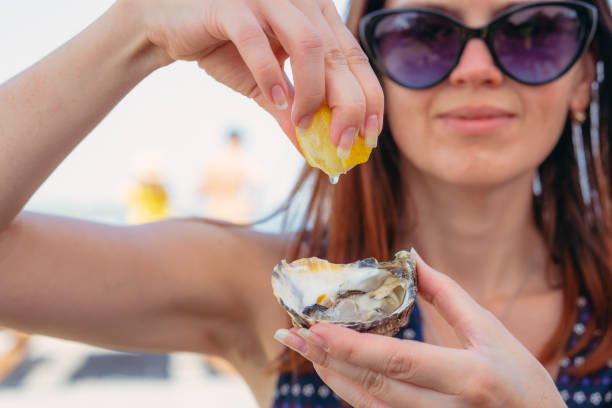 ostriche. una donna versa succo di limone su un'ostrica. - oyster foto e immagini stock