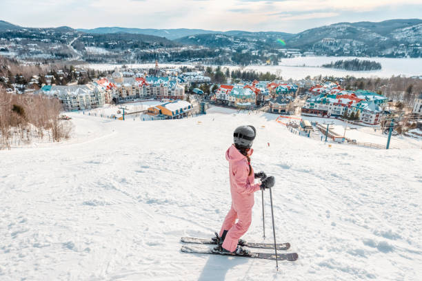 スキーの女性。アルペンスキー - スキーヤーは冬に雪に覆われたスキートレイルの斜面で下り坂を始める山村スキーリゾートの景色を見ています。カナダ ケベック州モントランブラン。 - sports helmet powder snow ski goggles skiing ストックフォトと画像