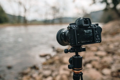A modern professional camera on a tripod, standing by a river and a beautiful landscape