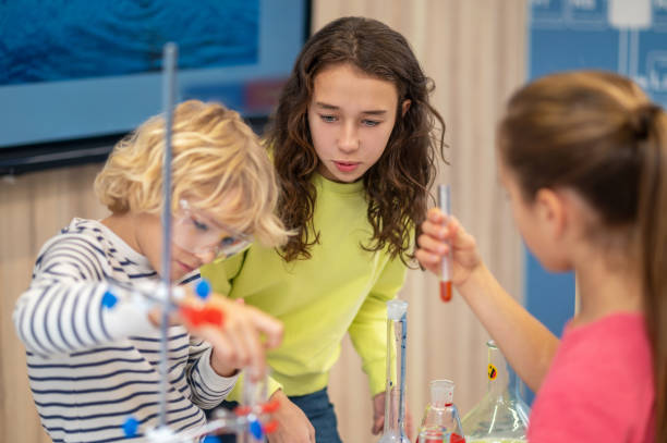 istock Girl with interest watching classmates with test tubes 1367212117