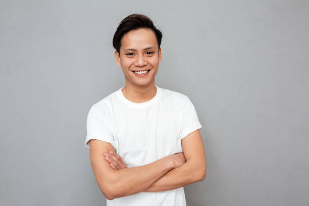 istock Happy asian man standing with arms crossed over grey wall. 1367212382