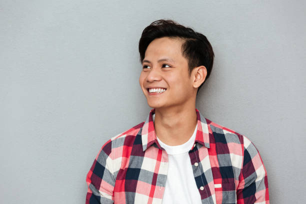 istock Young smiling asian man standing over grey wall. 1367212510