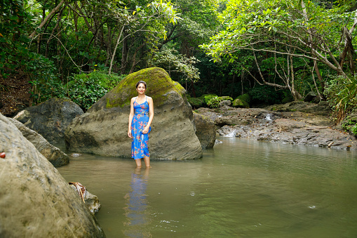 A woman in a blue dress wades in a shallow lagoon.  Costa Rica.  She is looking at the camera.