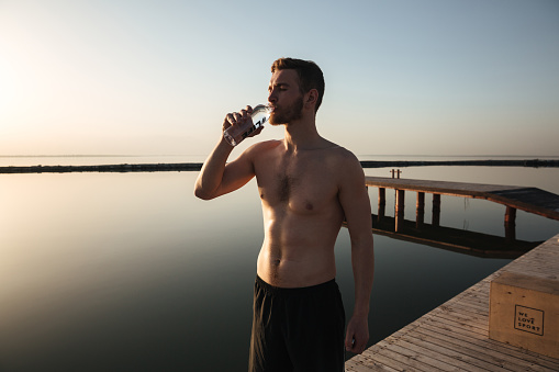 Portrait of a young tired sportsman drinking water after jogging outdoors