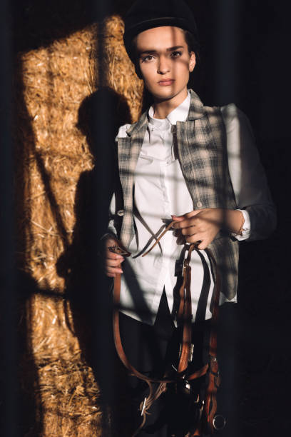 istock Concentrated young woman sitting in barn holding seddle 1367220124