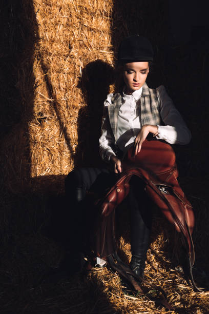 Serious young girl sitting in barn with seddle