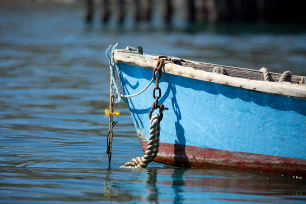 front of small blue row boat with anchor rope hanging off the front and disapearing in the calm watter stock photo
