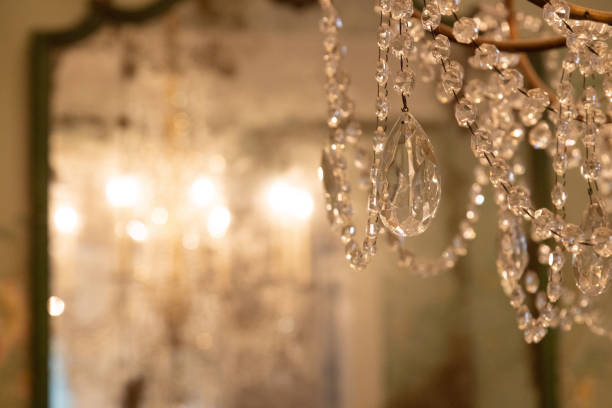 Clear, glass crystals hanging from chandelier reflecting brightly in decorative mirror stock photo