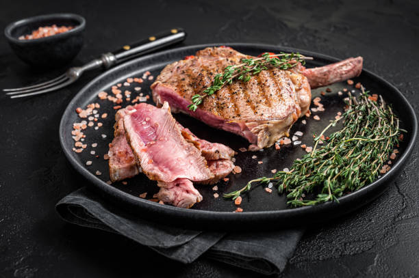 ピンクの塩とプレートにリブアイトマホークビーフ(子牛)ステーキをスライスバーベキュー。黒の背景。トップビュー - rib eye steak beef cutting board meat ストックフォトと画像