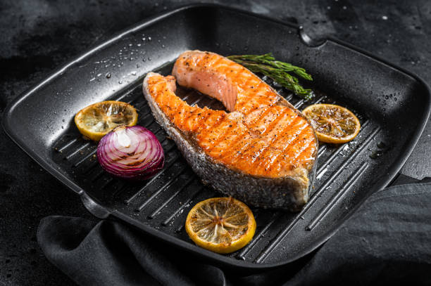 istock Salmon Fish Steak grilled on a grill pan with herbs. Black background. Top view 1367228252