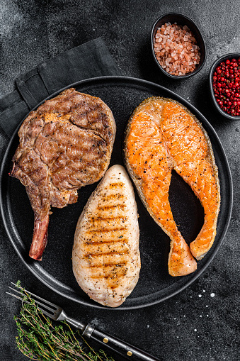 Grilled meat steaks - fish salmon, beef veal and turkey fillet.  Black background. Top view.
