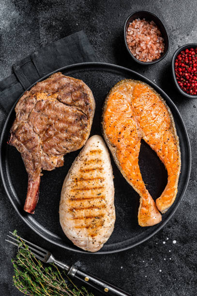 мясные стейки на гриле - рыбный лосось, говяжья телятина и филе индейки.  черный фон. вид сверху - barbecue meal seafood steak стоковые фото и изображения