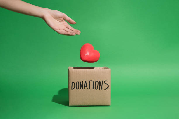 istock Levitating heart thrown by hand falling in charity donations box in green background 1367229101