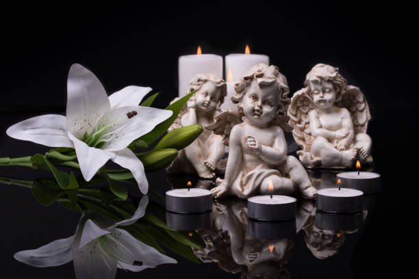 istock White angels with candles and white lily flower on a black background. 1367231777