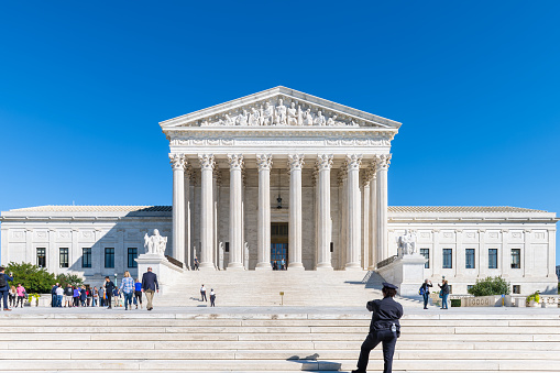 Washington DC, USA - October 12, 2018: People tourists and police woman standing by steps stairs of Supreme Court white stone marble building architecture and blue sky