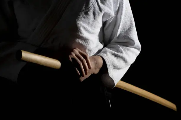 A girl in black hakama standing in fighting pose with wooden sword bokken Over dark background. Shallow depth of field. SDF.