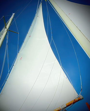Dreamlike, de-focused close up of sails against clear blue sky with the hint of a few clouds. Slight vignette, grainy, almost abstract design.