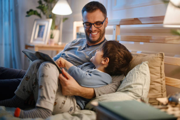 un jeune père lisant une histoire au coucher à son fils - bedtime photos et images de collection